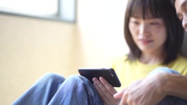Genç Japon çift akıllı telefondan video izliyor.
