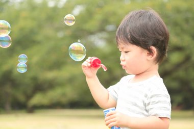Parkta sabun köpüğü üfleyen Asyalı küçük çocuk. 