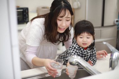 Küçük kızı olan genç Asyalı kadın bardaktan su içiyor.