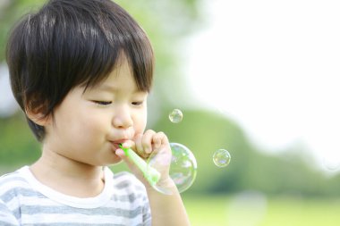 Parkta sabun köpüğü üfleyen Asyalı küçük çocuk. 