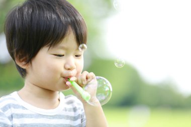 Parkta sabun köpüğü üfleyen Asyalı küçük çocuk. 