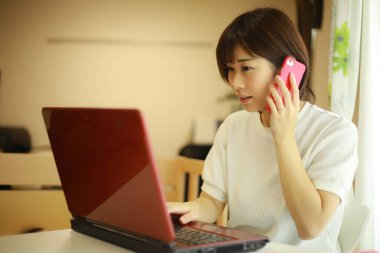 Genç Japon kadın evde çalışırken kırmızı laptop kullanıyor.