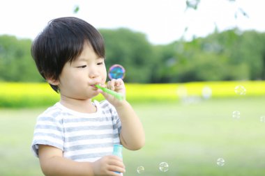 Parkta sabun köpüğü üfleyen Asyalı küçük çocuk. 