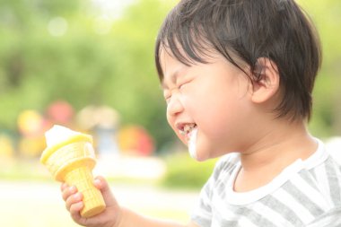 Parkta dondurma yiyen Asyalı küçük çocuk. 