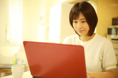 Genç Japon kadın evde çalışırken kırmızı laptop kullanıyor.