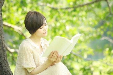 Parkta kitap okuyan Asyalı genç kadının portresi. 