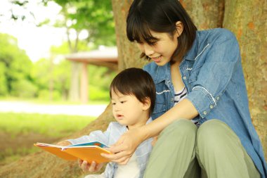 Genç Asyalı anne ve çocuğu parkta kitap okuyor.  