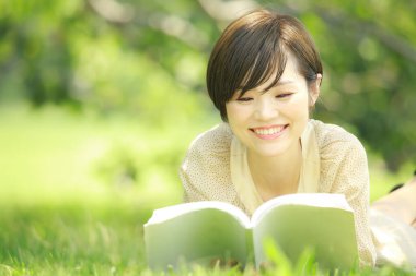 Parkta kitap okuyan Asyalı genç kadının portresi. 