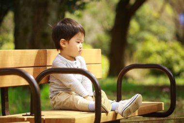 Küçük çocuk parkta bankta oturuyor.