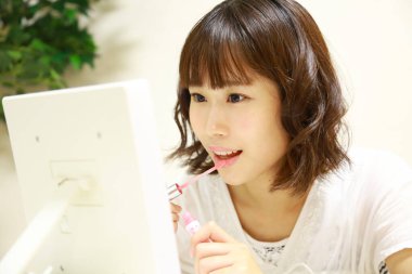 Genç Asyalı kadın aynaya makyaj yapıyor.