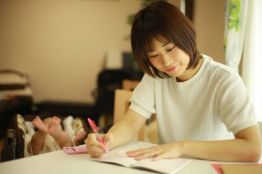 Genç Asyalı kadın evdeki deftere yazı yazıyor.