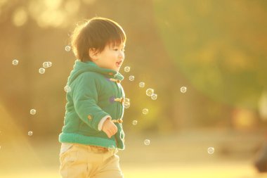 Parkta sabun köpüğü üfleyen Asyalı küçük çocuk. 