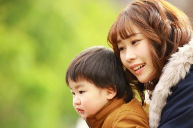 Genç Asyalı anne oğluyla parkta eğleniyor.  