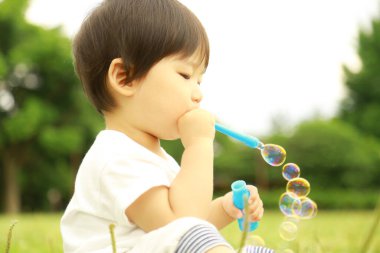 Parkta sabun köpüğü üfleyen Asyalı küçük çocuk. 