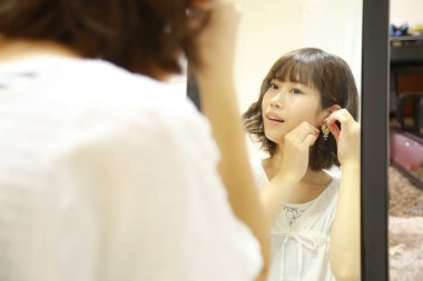 Genç Asyalı kadın aynaya makyaj yapıyor.