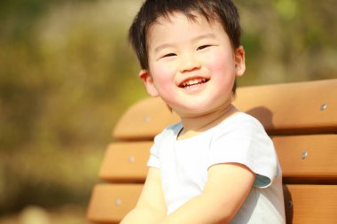 Küçük çocuk parkta bankta oturuyor.