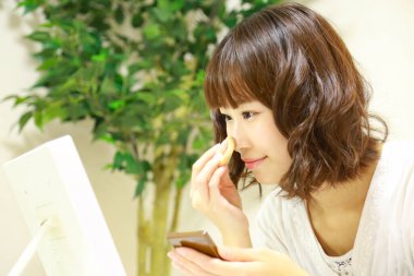 Genç Asyalı kadın aynaya makyaj yapıyor.