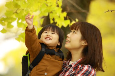 Küçük oğluyla birlikte genç Asyalı anne parktaki yapraklara bakıyor.  