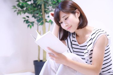 güzel genç Asyalı kadın evde kitap okuyor.