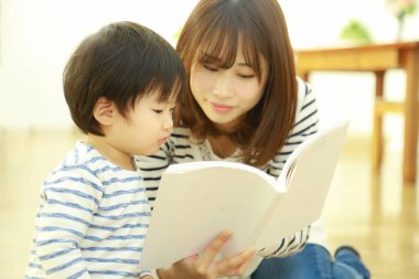 Küçük sevimli oğlu olan genç bir anne evde kitap okuyor.