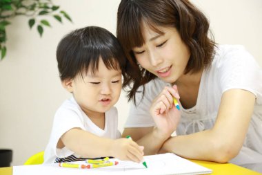 Anne ve oğul beyaz kağıda boya kalemleri çiziyor.