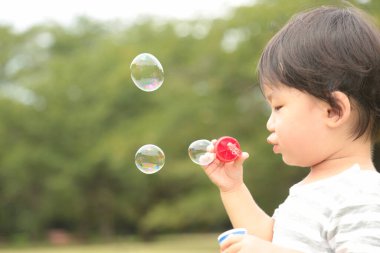 Parkta sabun köpüğü üfleyen Asyalı küçük çocuk. 