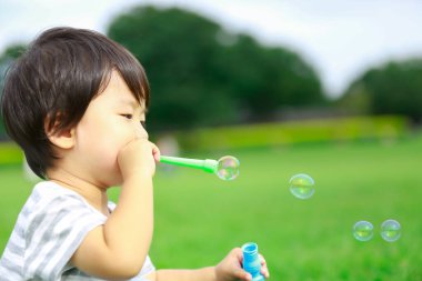 Parktaki tatlı Asyalı çocuk sabun köpüğü üflüyor. 