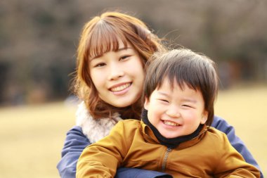 Genç Asyalı anne oğluyla parkta eğleniyor.  