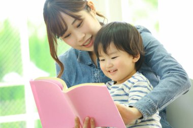 Küçük sevimli oğlu olan genç bir anne evde kitap okuyor.