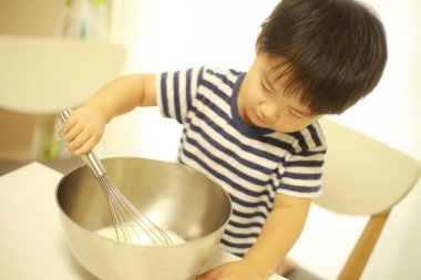 Küçük Asyalı çocuk mutfakta büyük bir karıştırma kabıyla yemek pişiriyor.