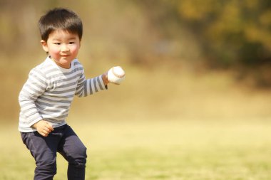 Küçük çocuk parkın arka planında topla oynuyor.