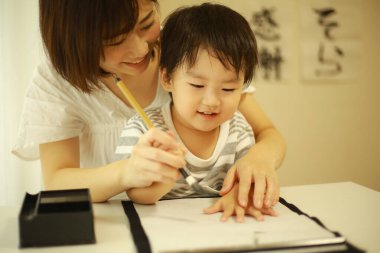 Anne ve oğul fırçayla yazı alıştırması yapıyorlar.