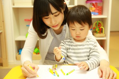 Anne ve oğul beyaz kağıda boya kalemleri çiziyor.