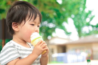 Parkta dondurma yiyen Asyalı küçük çocuk. 