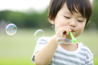 Parkta sabun köpüğü üfleyen Asyalı küçük çocuk. 