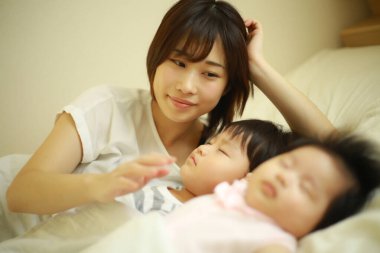 Mutlu Asyalı anne uyuyan oğlana ve kızına bakıyor 