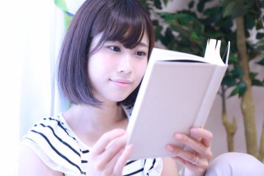 güzel genç Asyalı kadın evde kitap okuyor.