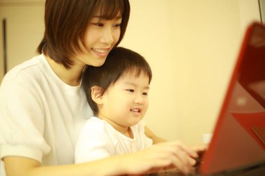 Asyalı genç kadın ve küçük oğlu dizüstü bilgisayar kullanıyor. 