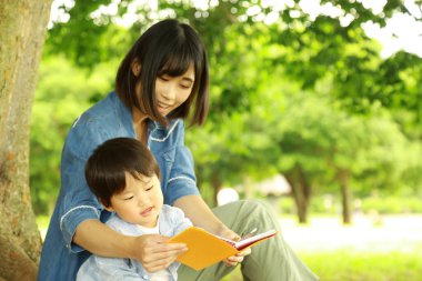 Genç Asyalı anne ve çocuğu parkta kitap okuyor.  