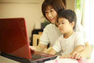 Asyalı genç kadın ve küçük oğlu dizüstü bilgisayar kullanıyor. 