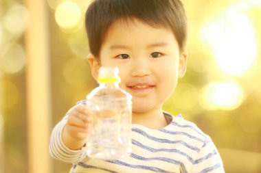 Yakışıklı, gülümseyen Asyalı çocuk elinde şişe tutuyor.