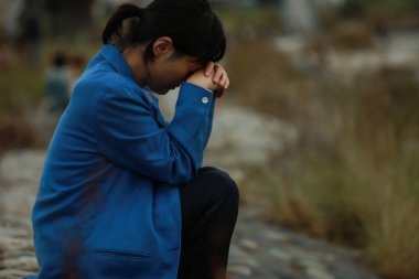 Üzgün ve yalnız Asyalı kadın nehir kenarında oturuyor.