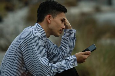 Üzgün ve yalnız Asyalı adam nehrin kenarında oturuyor.