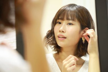 Genç Asyalı kadın aynaya makyaj yapıyor.