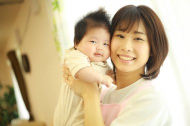 Asyalı genç anne, küçük tatlı kızını kucağında tutuyor. 