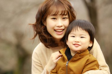 Genç Asyalı anne oğluyla parkta eğleniyor.  