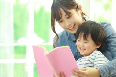 Küçük sevimli oğlu olan genç bir anne evde kitap okuyor.