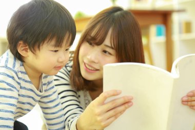 Küçük sevimli oğlu olan genç bir anne evde kitap okuyor.