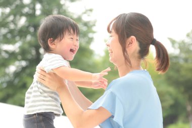 Genç Asyalı kadın parkta çocuğunu tutuyor.  