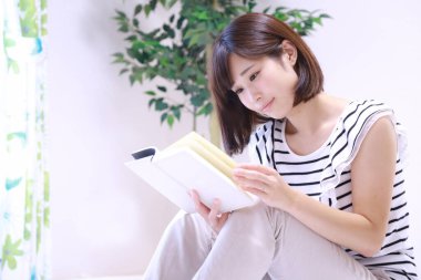 güzel genç Asyalı kadın evde kitap okuyor.